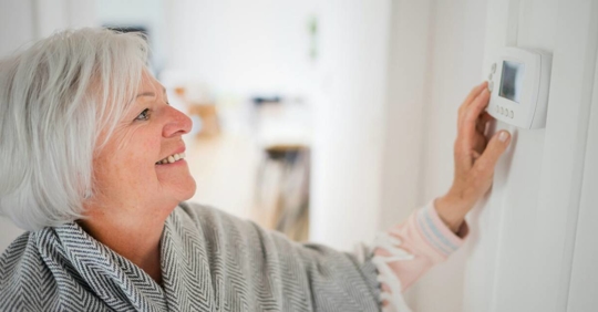 Senior woman adjusting her thermostat at home